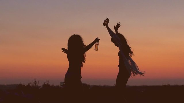 Female silhouettes celebrating and partying at music festival at sunset