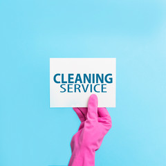 Female hand in pink gloves holds a card with text Cleaning services on a blue background. cleaning service concept. Flat lay, Top view