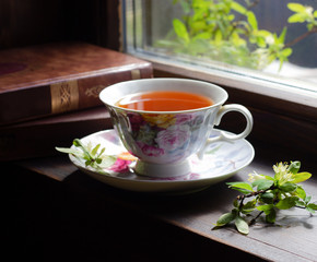 Cup of tea with blooming twig and books near window