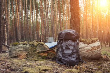 Tourist backpack, metal mug and map in the forest. Concept of a hiking trip to the forest or mountains