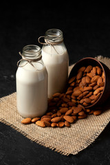almond milk in bottles with nuts on a dark black table, a variety of dairy products without sugar and lactose, a vegetarian drink