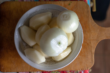Raw peeled potatoes and peeled onions in a plate
