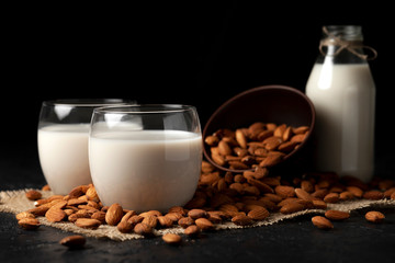 sugar-free and lactose-free almond milk in glasses and bottles with powdered nuts, vegetarian milk drink on a black table