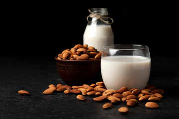 almond milk without sugar and lactose in glass with sprinkled nuts, vegetarian milk drink on a dark black table