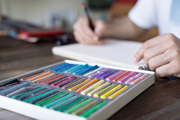 person, artist painting with a pastel crayon chalk on a white sheet of paper and pellette on the wooden table
