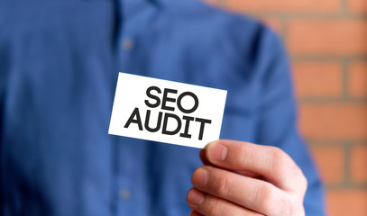 A man in a blue shirt holds a sign with the text of Seo audit n one hand