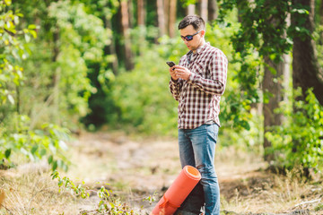 Hipster young man with backpack using smart phone on beautiful nature.Travel concept. Outdoor travel. Travel and explore. Backpacker male Going in forest Gps Route. Portrait hiker using mobile phone