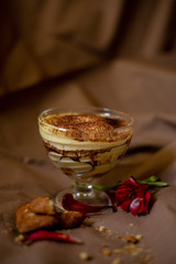 classic tiramisu cake in a beautiful glass form on a brown background, food photo, sweetness, festive dessert