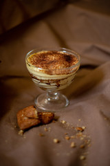 classic tiramisu cake in a beautiful glass form on a brown background, food photo, sweetness, festive dessert