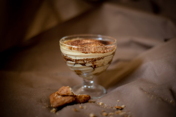 classic tiramisu cake in a beautiful glass form on a brown background, food photo, sweetness, festive dessert