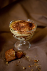 classic tiramisu cake in a beautiful glass form on a brown background, food photo, sweetness, festive dessert