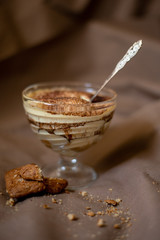 classic tiramisu cake in a beautiful glass form on a brown background, food photo, sweetness, festive dessert