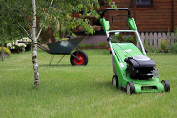 Fototapeta premium a green lawn mower standing on the lawn with a wheelbarrow in the background