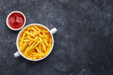 French fries with barbecue sauce, in a white bowl, against a dark background with place for text. top view