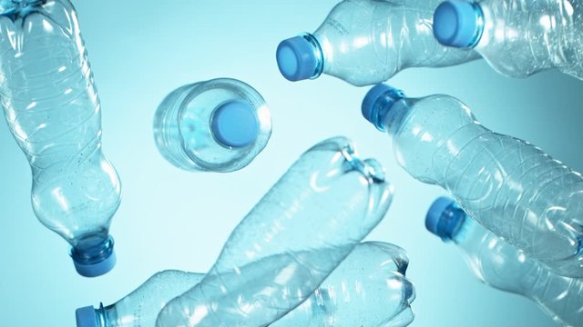 Super Slow Motion Shot of Flying Empty Plastic Bottles on Light Blue Gradient Background at 1000fps.