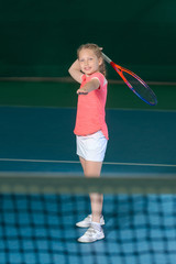 A girl plays tennis on an indoor tennis court.