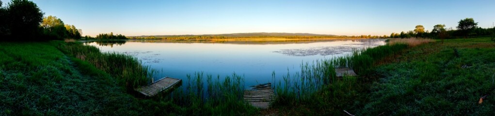 Panoramic landscape from the lake shore with colorful clouds in the spring sun.