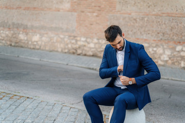 Young business man with white shirt and suit in outdoor city reaching for pocket in jacket