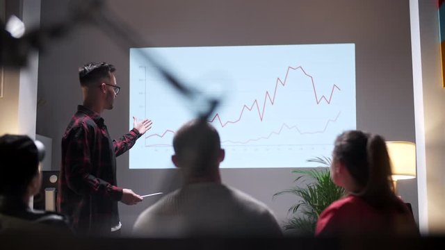 Business meeting. Office Team Analyzes Business Growth. Young Man Interested In Audience. On Screen Growth Graph Monitor
