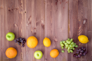 fruit on the bottom edge of a mocha wooden background. lemon, orange, grapefruit, red grapes, green grapes