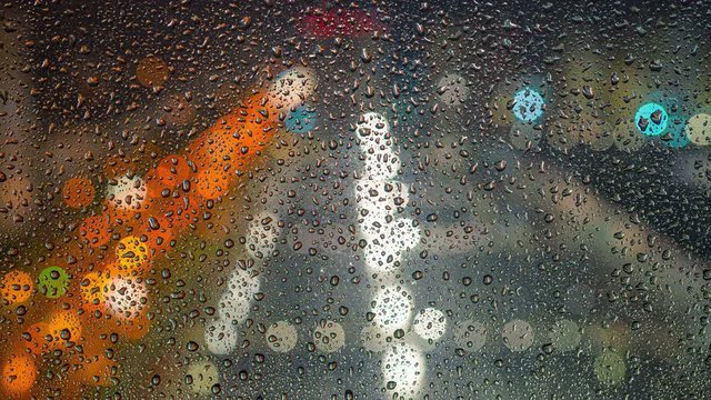 The rain drops flow down the glass on a background of city lights. time lapse