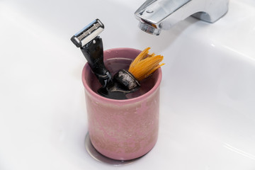 Male old used shaving kit in the wash basin. Shaving accessories in a glass
