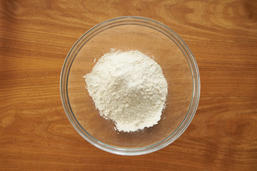 Pile of flour in a transparent glass salad bowl on wooden table top view