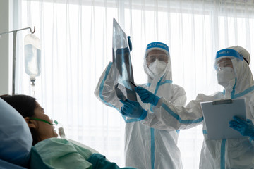 doctors in personal protective equipment or ppe looking at chest x-ray of the asian woman patient with covid-19 or coronavirus infection in the isolation unit in the hospital. medical concept