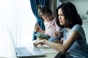 Asian young single mother using computer laptop for working from home and taking care little baby...