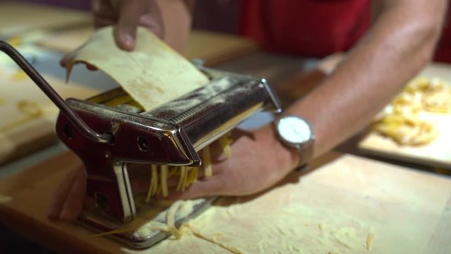 Slow motion of chef rolling appliance while making tagliatelle, people preparing pasta on kitchen counter - Tuscany, Italy