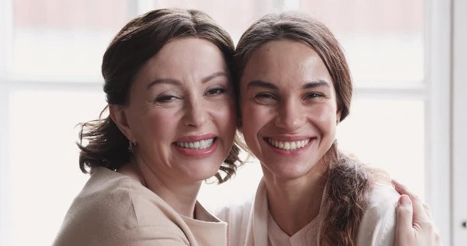 Head shot close up overjoyed smiling two bonding female generations family cuddling, looking at camera. Excited middle aged mommy enjoying funny tender moment, laughing with happy grown daughter.