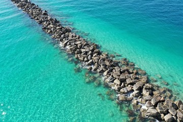 Aerial view of rock jetty of Government Cut surrounded by clear shallow water of Miami Beach, Florida on sunny summer morning.