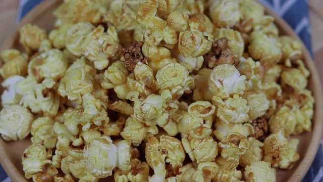 Caramel popcorn in a wooden plate  roating , Golden caramel popcorn closeup ,  Background of popcorn. Snacks and food for a movie 