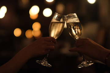 close up two hands holding drinking glass, cheers in darkness. Golden bokeh background