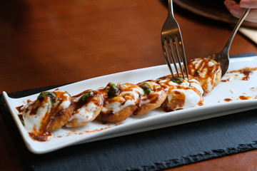 close up crispy fired potatoes topped with yoghurt and mint sauce. traditional Indian food. blur background