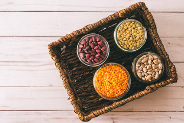 Red lentils, green lentils, small red beans, and pinto beans in bowls close up in wicker basket, view from above with copy space, vintage look.