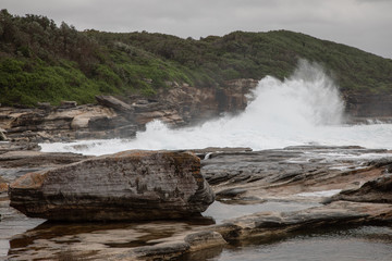 Storm in the ocean. Cloudy sky. Big waves are crashing into the rocks making white foam.