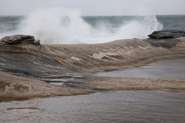 Storm in the ocean. Cloudy sky. Big waves are crashing into the rocks making white foam.