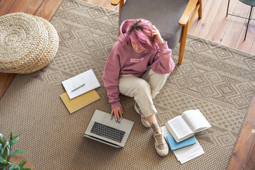 Young hipster teen girl school college student pink hair using laptop computer sit in cozy living...