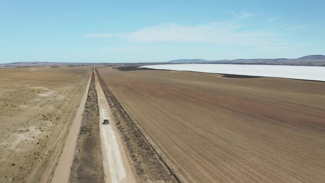 Aerial view on the black SUV car, driving along a dirt road next to the dried salt lake in the Australian outback.