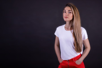 Fototapeta premium A young girl in a white t-shirt and red jeans on a black background. Copy space
