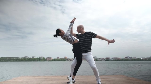 The couple in love dance social dance bachata pier on the lake, town horizon