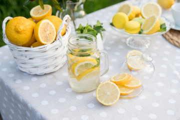 Lemonade with lemon, mint and ice on garden table. Preparation of the lemonade drink. Lemonade in the jug and lemons with mint on the table outdoor.