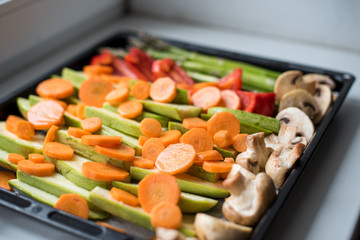 Mixed raw vegetables going to be roasted in the oven. Fresh vegetables on sheet pan. Colorful and delicious dish. Coating of oil is getting veggies crispy, roasty and tasty. Concept of healthy life.