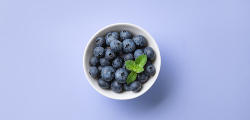 fresh juicy blueberries with mint in a white bowl on a blue background