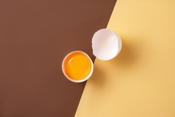 a fresh egg broken into two halves on a yellow and  brown background