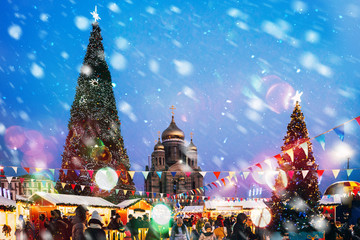 square with two Christmas trees and a church in the middle, in the foreground people, lights, it is snowing