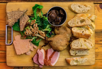 Gourmet platter with duck pate, foie gras, duck confit and seared duck breast on a wooden cutting board in a restaurant