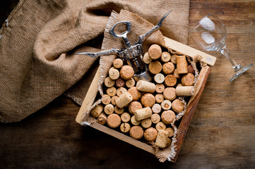 Wine corks of different sizes, a corkscrew, a bottle of wine and a glass shot on an old wooden surface. Background for liquor.