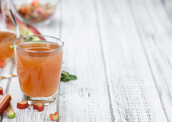 Old wooden table with fresh made Rhubarb Juice (close up; selective focus)